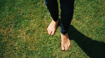 Person standing barefoot on the grass, connected to the earth to reap the benefits of earthing, or grounding, for physical and mental health