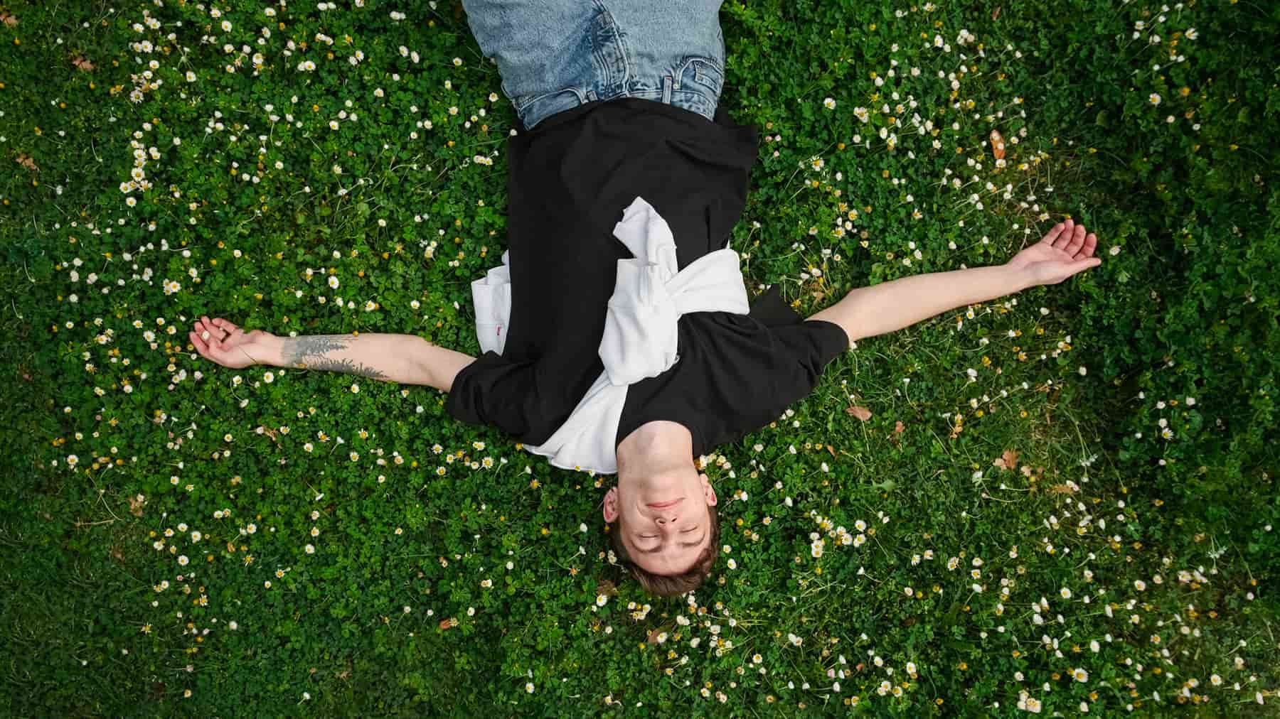 Modern young male lying on a beautiful grass field to recieve grounding benefits