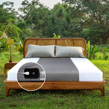 Gray grounding flat half-sheets arranged on a rustic wooden bed outdoors, surrounded by lush greenery, highlighting natural earthing techniques